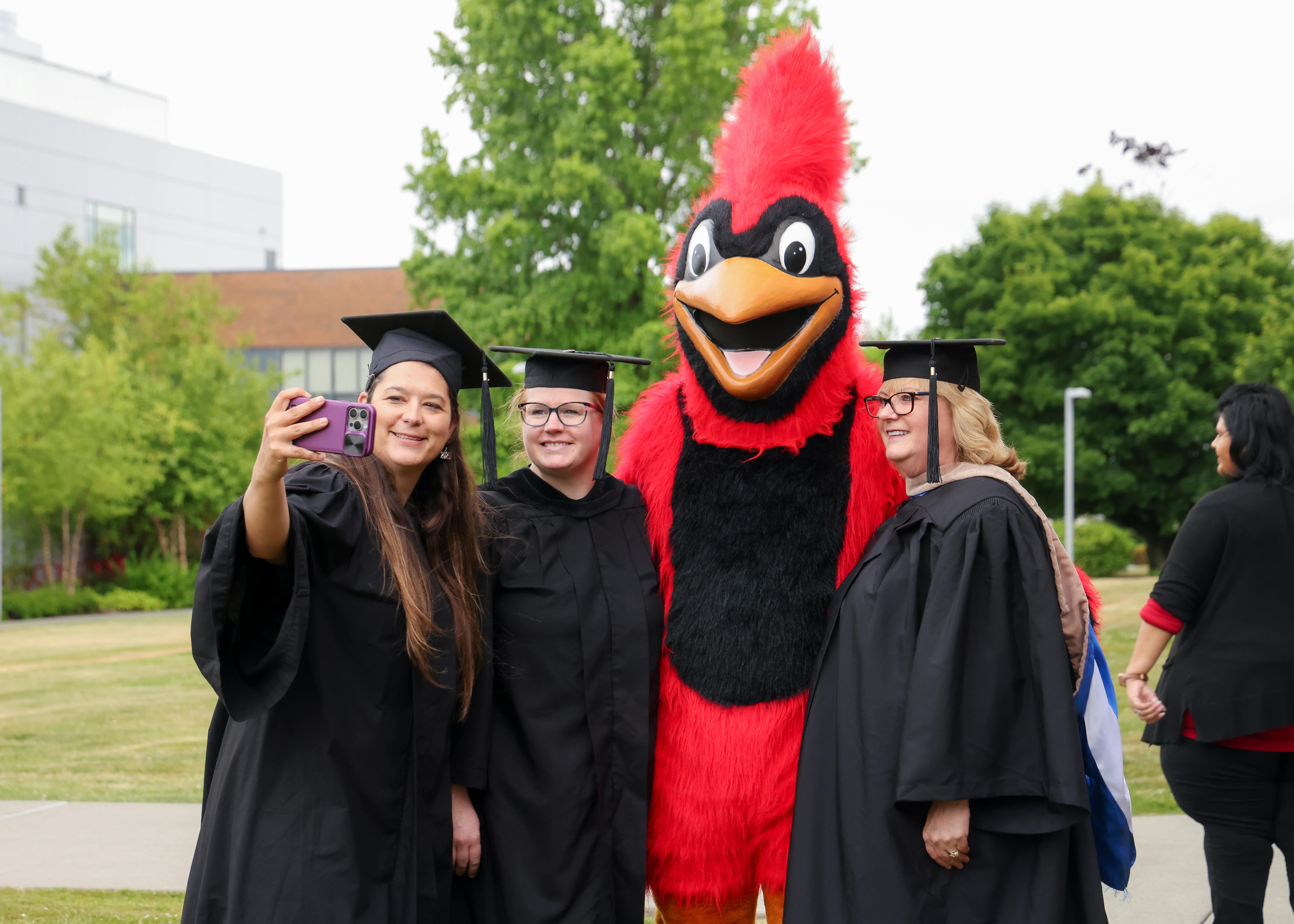 Bachelor's graduate taking a photo with parent and the cardinal bird after graduation
